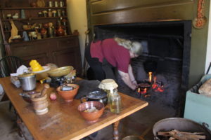 A Strawbery Banke staffer demonstrates 18th century open-hearth cooking in the restored kitchen of the c. 1780 Wheelwright House. There’s bacon in the pan she is placing over the fire.