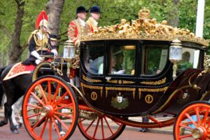 Queen Elizabeth II, seen waving a gloved hand, rides in her carriage to Parliament.