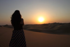 Abu Dhabi’s desert seen at sunset. I took this photo during a 2018 visit, not while riding in circles in a taxi!! The scene’s admirer at left is New York City-based journalist Hannah Freedman.
