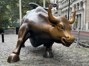The sculpture called “Charging Bull,” or the “Bull of Wall Street,” located at the north fringes of Bowling Green in Lower Manhattan. To be precise, as of 2016, the tiny northern tip of Bowling Green, location of the bull, was renamed Evacuation Day Plaza. The signage is visible in this photo behind the bull’s left horn. 